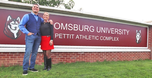 Steph '89 and Allie Pettit stand in front of a large sign that says "Bloomsburg University Pettit Athletic Complex"