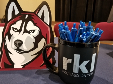 a Husky alumni sign sits on the RKL table next to company branded pens in a mug