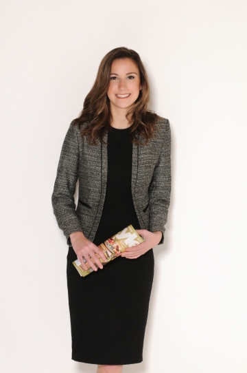 Kristen Wagner stands in front of a white background in a black dress and grey blazer, holding a rolled up Lehigh Valley Style magazine.