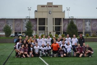 Field Hockey players and alumni gather on the field with Redman Stadium in the backdrop