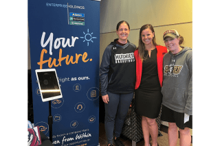 Kelsey Gallagher '12 stands with Husky Basketball coaches at a recent Career Connections Expo in front of a blue Enterprise Holdings roll-up banner