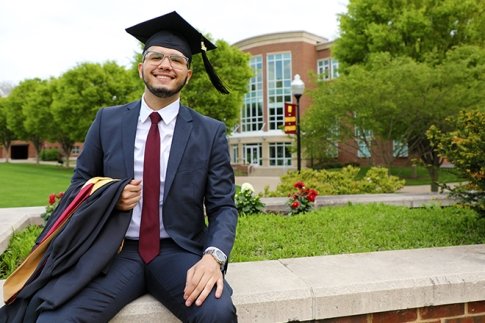 MBA graduate smiles while sitting on the Quad in front of Sutliff Hall