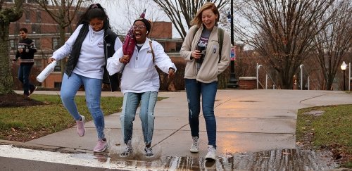 Friends jump in a water puddle for fun on their way across campus