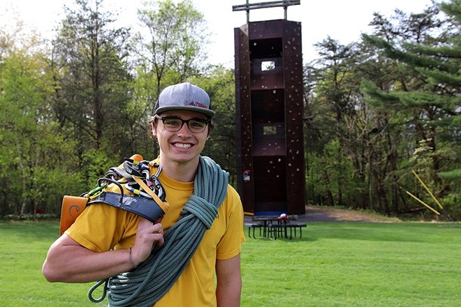 Anthropology major poses in front of the Quest climbing wall on upper campus